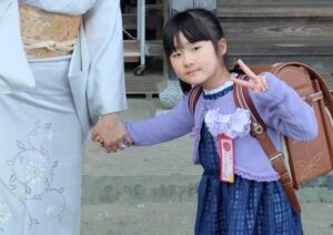 母と手をつなぎランドセルを背負い入学式の服でピースをする小倉美咲